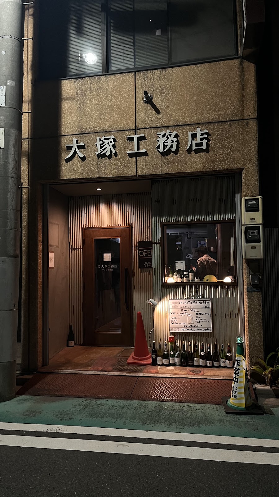夜の店舗外観。大塚工務店の看板の下にOPENサインが灯る